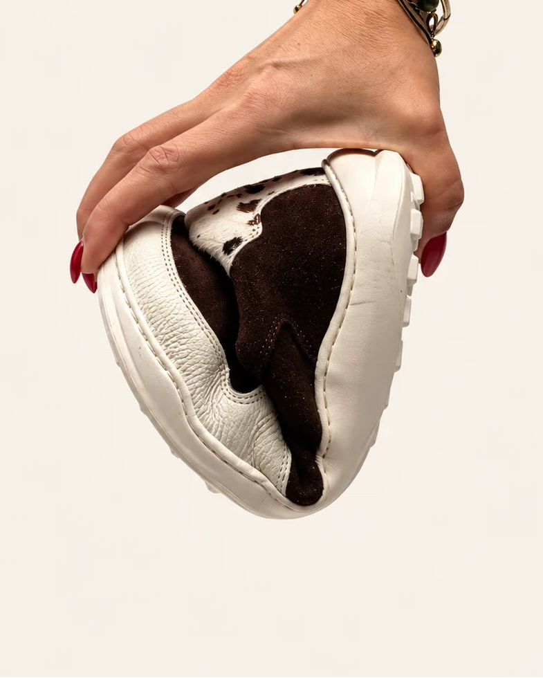 Mano doblando la deportiva barefoot de transición LÍA chocolate y vaca para mostrar la flexibilidad de su suela