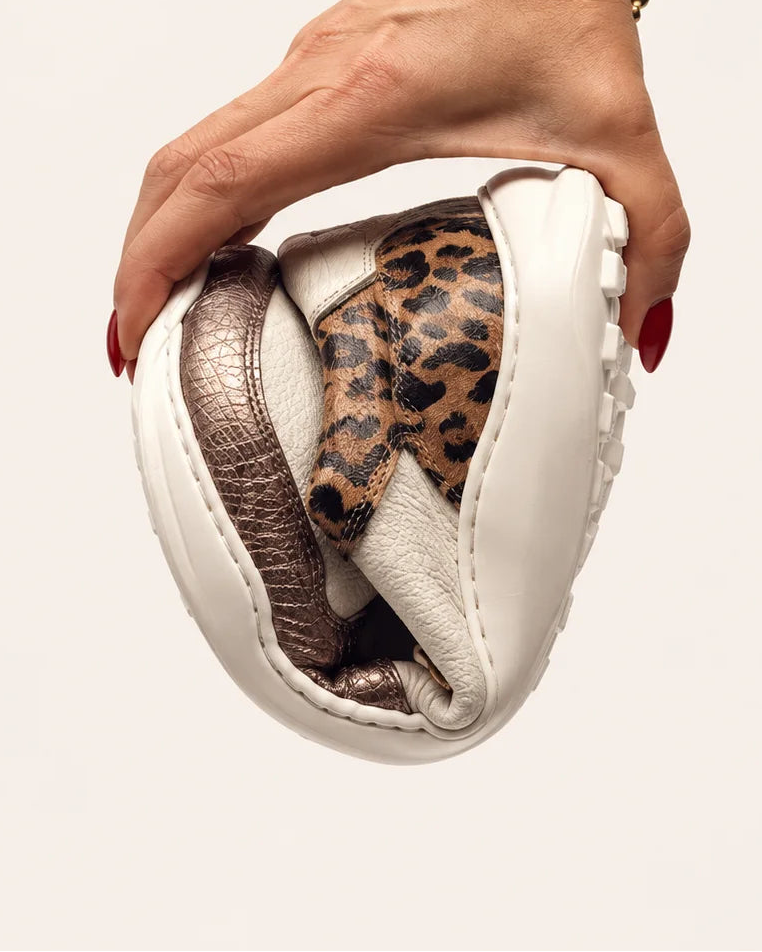 Mano doblando la deportiva barefoot de transición de mujer modelo LÍA en piel marfil y leopardo de Valenta Unic para mostrar la flexibilidad de su suela