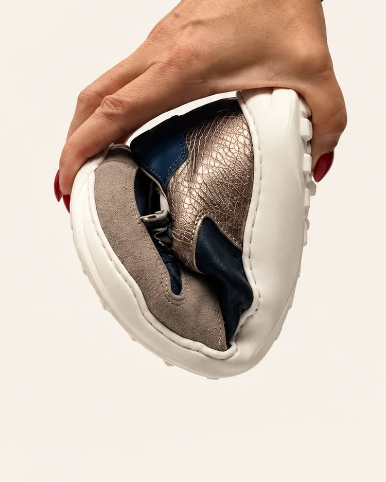 Mano doblando la deportiva barefoot de transición de mujer modelo LÍA mediterraneo en piel combinando azules de Valenta Unic para mostrar la flexibilidad de su suela