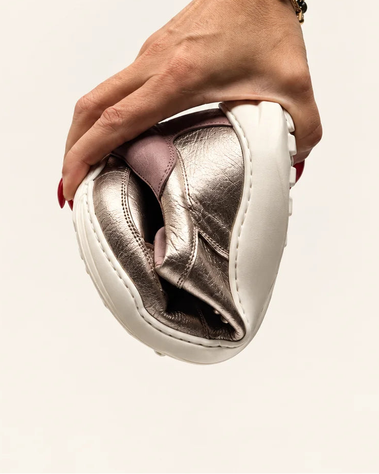 Mano doblando la deportiva barefoot de transición de mujer modelo LÍA en piel oro y rosa de Valenta Unic para mostrar la flexibilidad de su suela