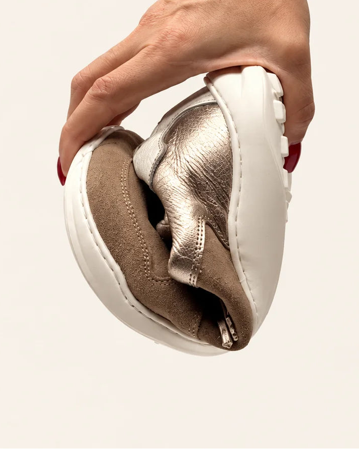 Mano doblando la deportiva barefoot de transición de mujer modelo LÍA sand en piel serraje camel y oro de Valenta Unic para mostrar la flexibilidad de su suela
