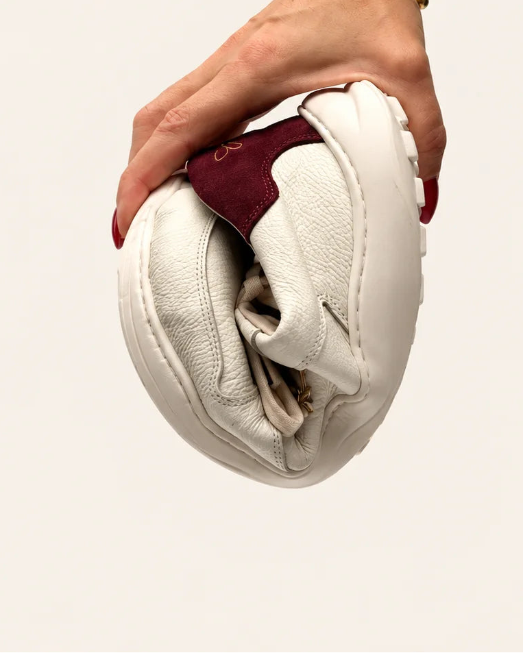 Mano doblando la deportiva barefoot de transición casual de hombre Leo ivory piel nata y burdeos para mostrar la flexibilidad de su suela